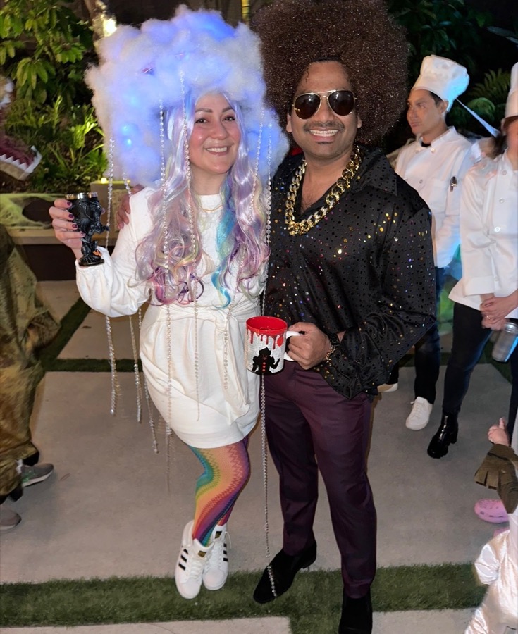 Two people posing in colorful costume at an outdoor party.